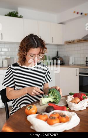 Junge Frau, die zu Hause Gemüse in der Küche schneidet Stockfoto