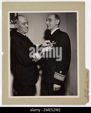 Konteradmiral Spencer wurde mit der Verdienstlegion ausgezeichnet. Vizeadmiral Russell R. Waesche (links), Befehlshaber der USA Küstenwache, überreicht die Legion of Merit Medaille an Konteradmiral Lyndon Spencer, USA Küstenwache, die wie folgt zitiert wurde: "Für außergewöhnlich verdienstvolle Dienste als kommandierender Offizier der USS Bayfield für ihre erfolgreichen Einsätze bei der Landung von Armeetruppen auf der französischen Halbinsel Cherbourg gegen gut vorbereitete Verteidigung und starke Opposition im Zeitraum vom 6. Bis 24. Juni 1944." Konteradmiral Spencer, der vor kurzem vom Captain aufgezogen wurde und jetzt Assistant Operations ist Stockfoto