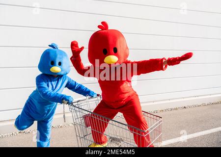 Eine Frau in einem roten Entenkostüm, die Spaß mit einem Mann hat, der einen Einkaufswagen schiebt Stockfoto
