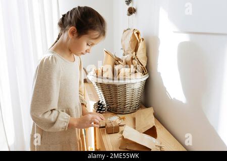 Süßes Mädchen, das Geschenke aus Adventskalender auf einem Schrank zu Hause öffnet Stockfoto