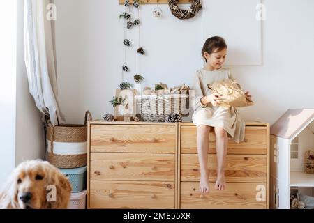 Lächelndes Mädchen mit Geschenk, das zu Hause im Schrank sitzt Stockfoto
