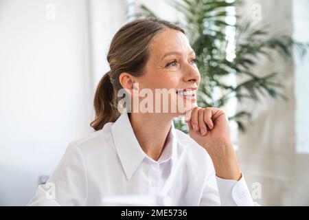 Rücksichtsvolle, reife Geschäftsfrau mit Hand am Kinn im Büro Stockfoto