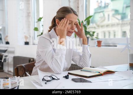 Frustrierte Geschäftsfrau mit Kopf in den Händen, die im Büro sitzt Stockfoto