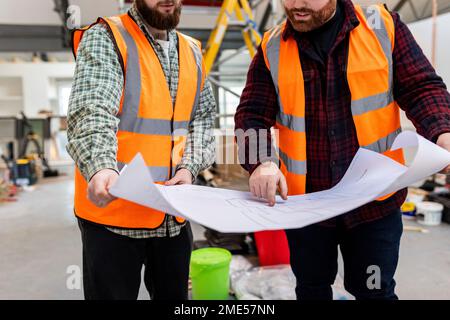 Ingenieure in reflektierender Arbeitskleidung diskutieren über Baupläne auf der Baustelle Stockfoto