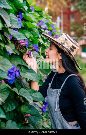Glückliche Frau mit Hut, die Blumen im Garten berührt Stockfoto
