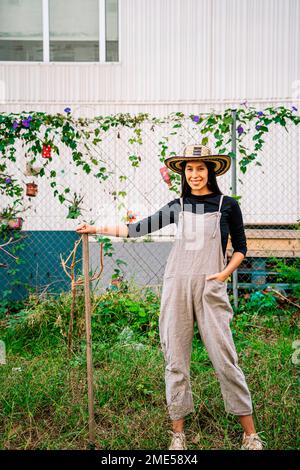 Glückliche junge Frau, die mit Rechen im städtischen Garten steht Stockfoto