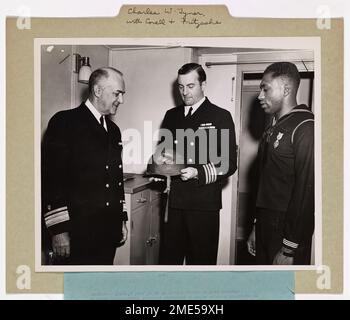 Bay State Coast Guardsman verlieh Purple Heart für Wunden in Frankreich. Küstenwächter Charles W. Tyner (rechts) Feuerwehrmann erster Klasse von West Medford, Mass., erhält den Purple Heart Award für Wunden, die bei der Invasion der Riviera von Südfrankreich erlitten wurden. Konteradmiral Leon C. Covell (RET) gab die Präsentation in Gegenwart des Küstenwachetransfers E. H. Fritzsche (Center), der Tyners Helm mit der Kugel untersucht. Küstenwachmann Tyner wurde bei der ersten Wellenlandung verwundet. Er dient an Bord eines von der Küstenwache bemannten Invasionstransports, dessen Kapitän Fritzsche Kapitän ist. Tyners Haus ist eine Stockfoto