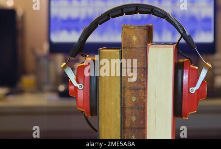 Hörbuchkonzept mit Bücherzeile und klassischen Kopfhörern, verschwommene Wellenform auf einem Computer im Hintergrund Stockfoto