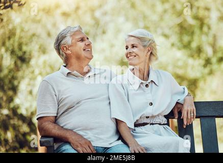 Liebe, Ruhestand und ein Paar auf einer Bank im Park mit Lächeln, Entspannung und Zeit in der Natur zusammen. Romantik, Seniorin und Rentnerin Stockfoto
