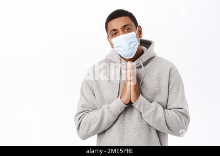 Covid Awareness, Gesundheitskonzept. Bild eines besorgten afroamerikanischen Mannes in medizinischer Maske, flehend Sie, flehend mit hoffnungsvollem Blick, weiß Stockfoto