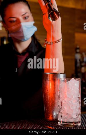 Junge Barkeeperin macht einen Cocktail mit Gesichtsmaske Stockfoto