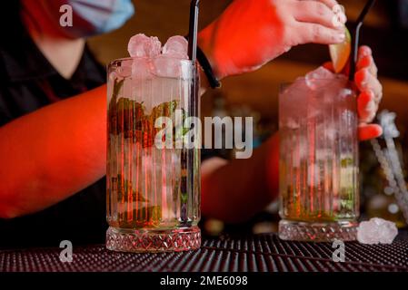 Junge Barkeeperin macht einen Cocktail mit Gesichtsmaske Stockfoto