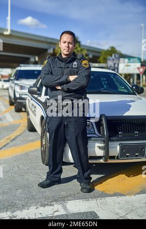 Ich bin entschlossen, Verbrechen auszurotten. Das ganze Porträt eines gutaussehenden jungen Polizisten, der auf Patrouille mit gekreuzten Armen stand. Stockfoto