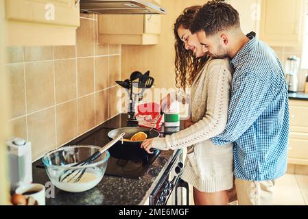 Er sorgt dafür, dass alles perfekt wird. Ein junges Paar, das zusammen in der Küche arbeitet. Stockfoto