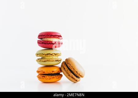 Ein Stapel roter Samt-, Pistachio-, Schokoladen- und Mandarinenkekse und Milchschokolade-Makkaron-Kekse auf weißem Hintergrund Stockfoto