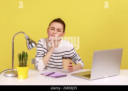 Unzufriedene Büroangestellte, die die Wange mit den Fingern berührt, unangenehme Zahnschmerzen nach dem Kaffeetrinken, Zahnprobleme. Studioaufnahmen im Innenbereich isoliert auf gelbem Hintergrund. Stockfoto