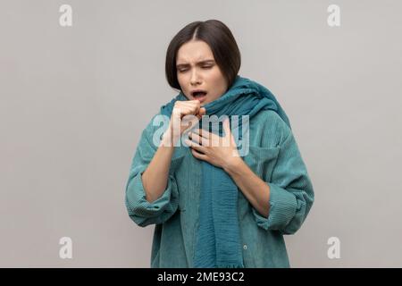 Portrait der Frau eingewickelt in warmen Schal, Husten, Unwohlsein leiden Fieber, saisonale Grippe Symptome, tragen lässige Jacke. Studioaufnahmen im Innenbereich isoliert auf grauem Hintergrund. Stockfoto