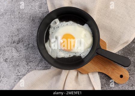 Gebratene Eier auf einer gusseisernen Pfanne auf einem kleinen Schneidebrett auf dunkelgrauem Hintergrund. Draufsicht, flach liegend Stockfoto