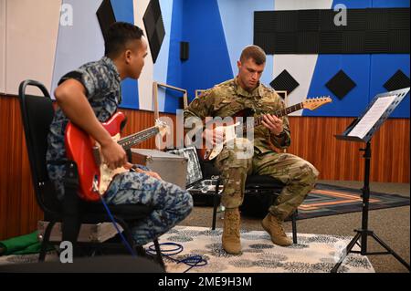 USA Air Force Master Sgt. Dustin Trimble, Lead Gitarrist der US Air Force Band of the Pacific, zeigt Royal Malaysian Air Force Gitarrist Lance CPL. Owen anak Ajew ein paar Gitarrenriffs während einer Pause zwischen den Übungseinheiten am Subang Air Base, Malaysia, 15. August 2022. Im Rahmen der Übung Pacific Angel 22 kamen Bandmitglieder aus drei teilnehmenden Ländern zusammen, um zu üben, voneinander zu lernen und gemeinsam zu arbeiten. Stockfoto