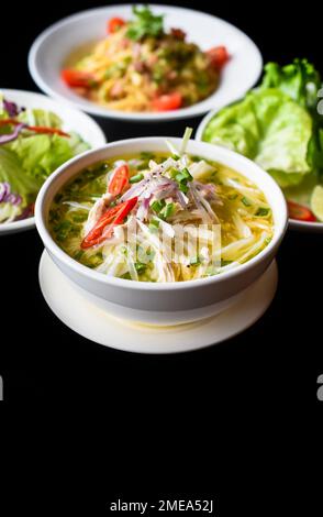 Hühnersuppe Pho ga im vietnamesischen Stil auf schwarzem Hintergrund mit Banh mi Brot, Salat und Pasta Carbonara Stockfoto