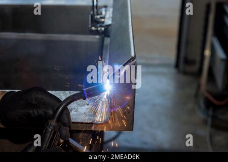 Arbeiter schweißen Metall mit Glitzereffekt mithilfe einer halbautomatischen Argon-Gas-geschirmten Schweißmaschine, um Metalle zu verbinden Stockfoto