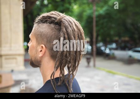 Rückblick auf einen Weißen mit Dreadlocks und Seitenrücken auf einer Sommerstraße Stockfoto