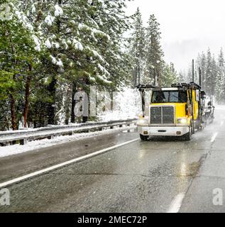 Klassischer amerikanischer Transporter für industrielle Zwecke mit gelbem Day Cab und großem Lkw mit leerem modularem hydraulischem Auflieger auf dem Stockfoto