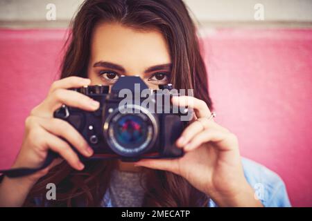 Durch die Stadt zu gehen, nur mit ihrer Kamera. Porträt einer schönen jungen Frau, die eine dslr-Kamera hält und draußen gegen eine Wand posiert. Stockfoto