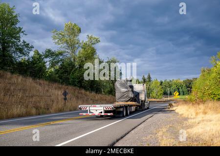 Industriequalität Hochkabinen amerikanischer leistungsstarker, klassischer, weißer Sattelzugmaschine für den Transport von abgedeckter gewerblicher Fracht auf einem Auflieger mit Abwärtsbewegung Stockfoto