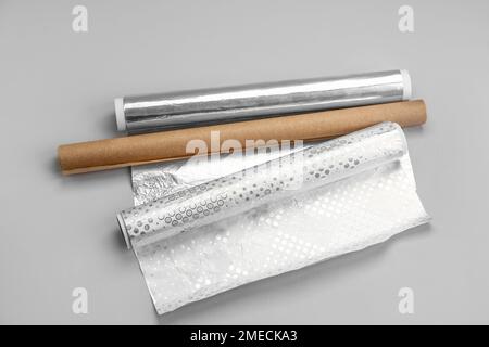 Rollen aus Aluminiumfolie und Backpapier auf grauem Hintergrund Stockfoto