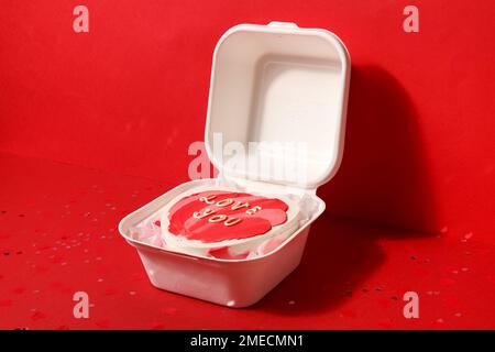 Lunchbox mit herzförmigem Bento-Kuchen zum Valentinstag auf rotem Hintergrund Stockfoto