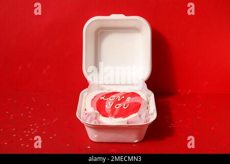 Lunchbox mit herzförmigem Bento-Kuchen zum Valentinstag auf rotem Hintergrund Stockfoto