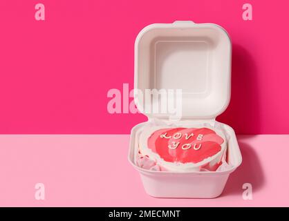 Lunchbox mit herzförmigem Bento-Kuchen zum Valentinstag auf pinkfarbenem Hintergrund Stockfoto