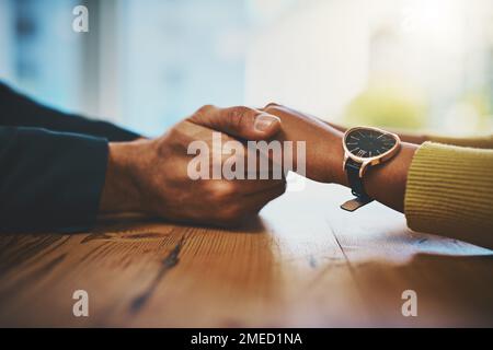 Sie befinden sich jetzt in einem sicheren Raum. Ein Mann und eine Frau, die mitfühlend Händchen an einem Tisch halten. Stockfoto