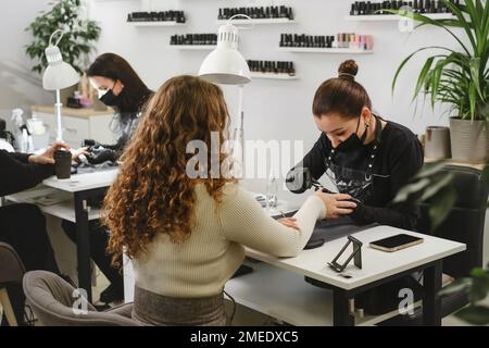 Maniküre im Salon. Maniküre-Maniküre-weiblich an Klientennägeln im Salon. Berufsbegriff. Kunden des Beauty Green Modern Studios Stockfoto