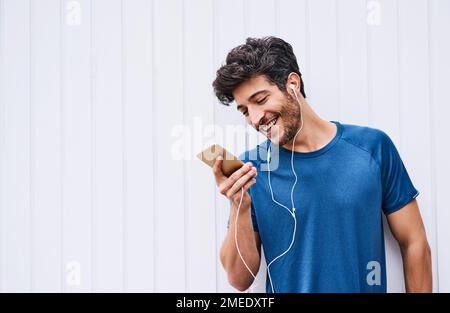 Die richtigen Melodien sorgen für die richtige Stimmung für ein großartiges Workout. Ein sportlicher junger Mann, der beim Sport im Freien Musik hört. Stockfoto