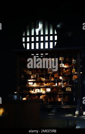 Eine vertikale Aufnahme von Licht, das auf die traditionelle japanische ema in einem dunklen Laden scheint Stockfoto