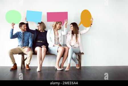 Weißt du, was ich denke? Eine Gruppe von Arbeitskollegen, die nebeneinander sitzen und Sprechblasen vor weißem Hintergrund halten. Stockfoto