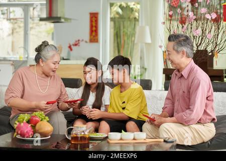 Großeltern, die ihren Enkeln bei der Tet-Feier Glücksgeld-Umschläge geben Stockfoto
