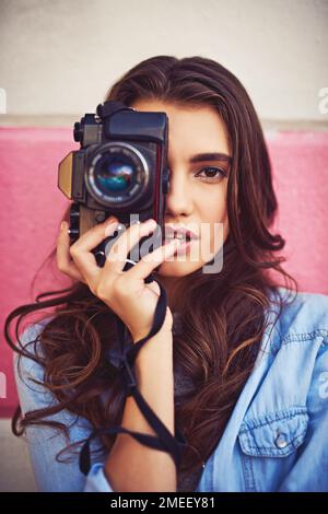 Sie nimmt ihre Kamera überallhin mit, um Erinnerungen festzuhalten. Porträt einer schönen jungen Frau, die eine dslr-Kamera hält und draußen gegen eine Wand posiert. Stockfoto