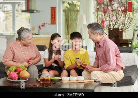 Großvater und Großmutter geben ihren Enkeln rote Glückssumschläge für Tet Stockfoto