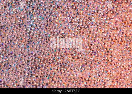 Abstrakter Strasssteinhintergrund. Textur von Strasssteinen, die mit mehrfarbigem Licht beleuchtet werden. Rosa und blaue glänzende Diamanten. Schließen. Leuchtfackeln auf Glas. Stockfoto