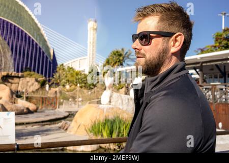 Porträt eines lächelnden Mannes mit Sonnenbrille, der in die Straßen der Stadt blickt. Stockfoto