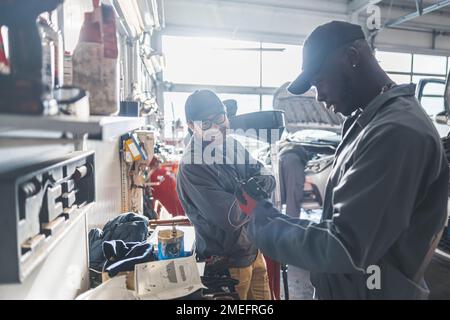 Mittlere Aufnahme. Zwei männliche Mechaniker arbeiten zusammen, von einer Wokrbank und lächeln. Werkstattkonzept. Hochwertiges Foto Stockfoto