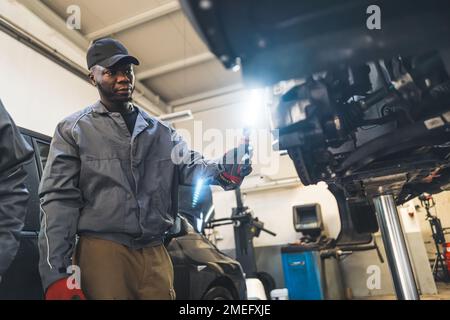 Mittlere Aufnahme eines Mechanikers, der ein Auto mit einem Licht überprüft. Werkstattkonzept. Hochwertiges Foto Stockfoto