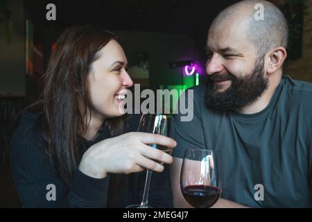 Glückliches junges Paar, das Wein trinkt, genießen Sie ein romantisches Abendessen zusammen im Luxusrestaurant. Ein bärtiger Mann sieht seine schöne Frau brünette Frau liebevoll an. Stockfoto
