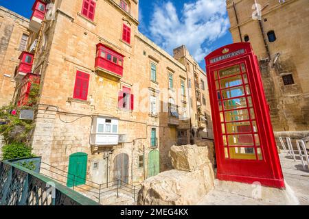 Valletta, Malta – Alte Straße von Valletta mit einer berühmten britischen roten Telefonzelle und traditionellen Balkonen und blauem Himmel an einem sonnigen Sommertag Stockfoto