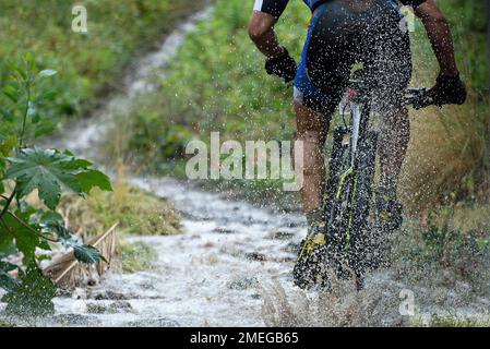 Mountainbiker fahren bei Regen flussaufwärts Stockfoto