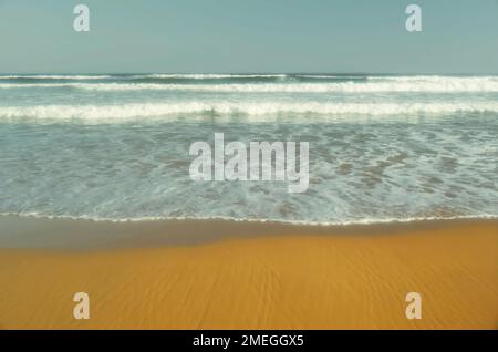 Ankommende Wildwasserwellen, die auf einen Sandstrand Rollen Stockfoto