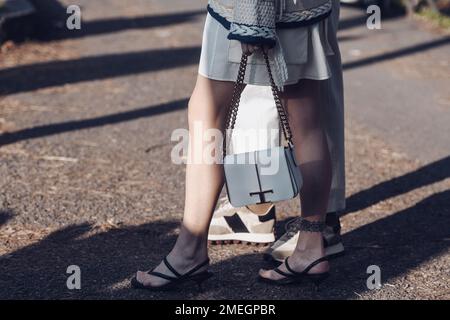 Mailand, Italien - 24. Februar 2022: Crop Woman in gestricktem Pullover Rock und Sandalen mit Kettentasche in der Nähe eines Mannes mit weißen Hosen und Turnschuhen Stockfoto